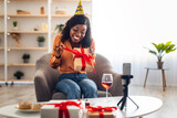 Black Woman Opening Birthday Gift In Front Of Smartphone Indoors