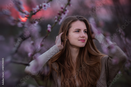 Young millennial woman in pink blooming sakura gardens at red sun sunset. Close-up portrait