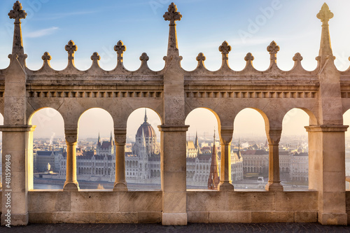 View through the columns of the Fishermen Bastion to the Parliament building at the Danube River in Budapest, Hungary, during golden sunrise time