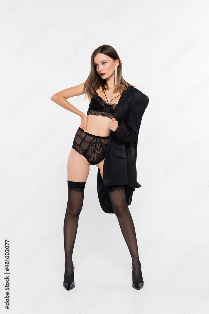 seductive woman in lace lingerie and black stockings posing with hand on hip and black blazer on grey. seductive woman in lace lingerie and black stockings posing with hand on hip and black blazer on grey.
