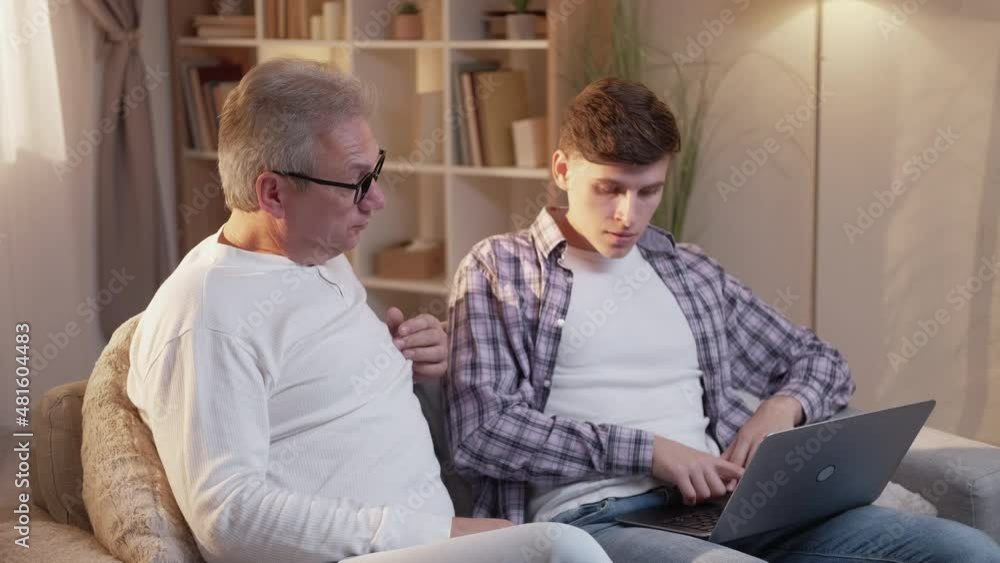 Parent helping son. Laptop leisure. Family home. Supportive father teaching teen student how to use internet computer program on sofa at living room. Parent helping son. Laptop leisure. Family home. Supportive father teaching teen student how to use internet computer program on sofa at living room.