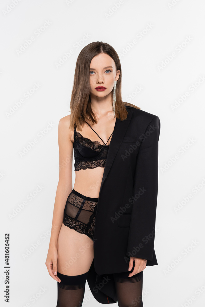 sexy woman in black lace underwear looking at camera while posing with black blazer isolated on grey.