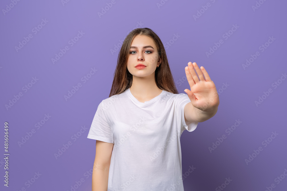Displeased girl saying NO, showing rejection gesture, expressing her negative attitude, wears blank white t shirt, standing over purple background. Stay home.Social distancing.New normal behavior Displeased girl saying NO, showing rejection gesture, expressing her negative attitude, wears blank white t shirt, standing over purple background. Stay home.Social distancing.New normal behavior