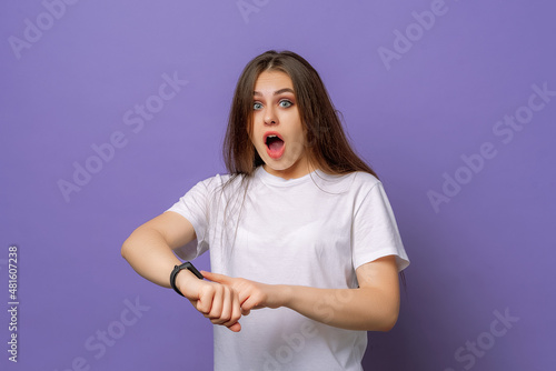 Too late, hurry up. Young beautiful brunette woman in hurry pointing finger on wrist watch, impatience, upset and angry for deadline delay. Studio shot, purple background