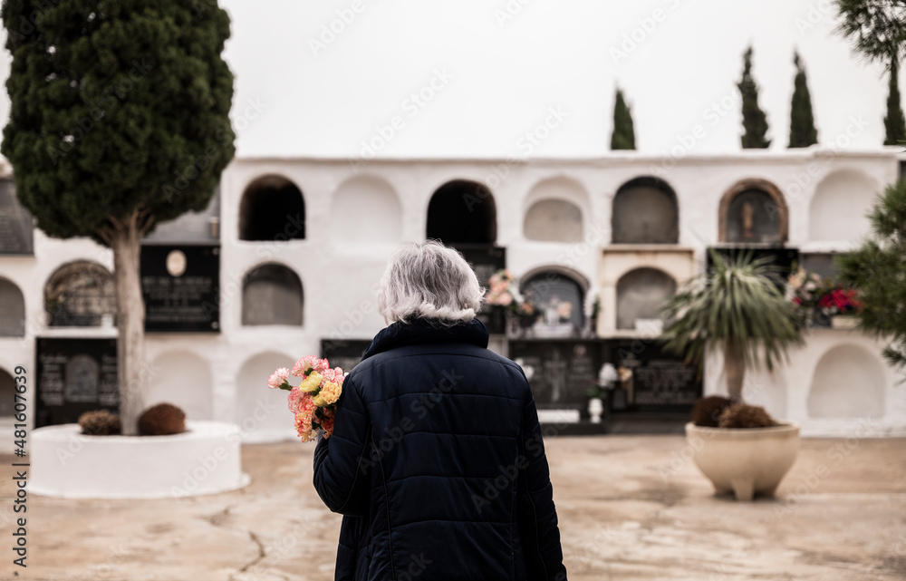 Rear view of woman holding flowers and mourning her family in cemetery. Almeria, Spain