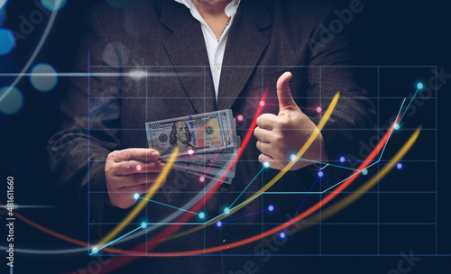 businessman in a suit holds a pack of paper american dollars against the background of a holographic chart with growing indicators. The concept of high business profitability, income growth
