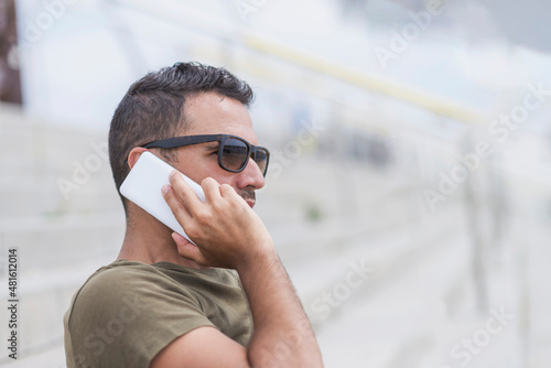 Happy man in sunglasses standing outdoors, talking by smartphone photo