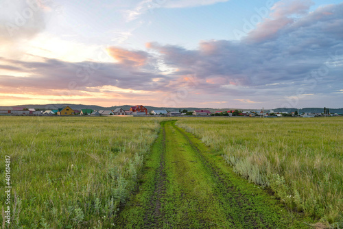 Dirt road leading to the village in summer on the background of sunset