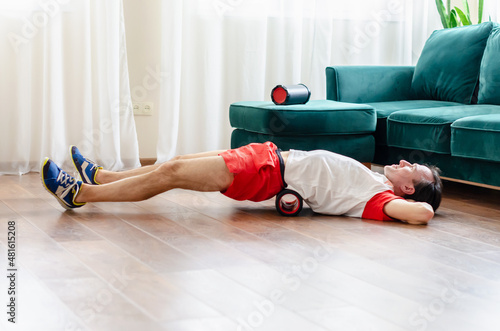 A young man in red shorts is doing exercises on a foam roller, works out of the muscles with a massage roller. Athletic man using a foam roller to relieve sore muscles after a workout