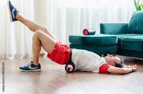 A young man in red shorts is doing exercises on a foam roller, works out of the muscles with a massage roller. Athletic man using a foam roller to relieve sore muscles after a workout