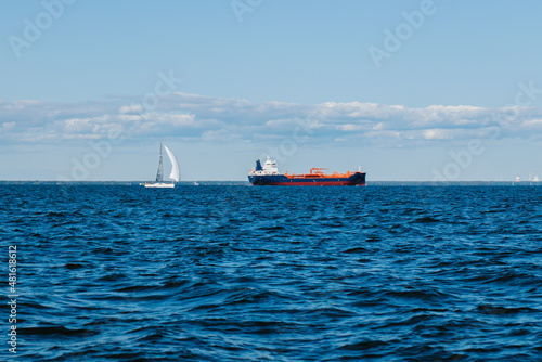 Tableau sur toile A view from the water of the Gulf of Finland on a summer day, cargo ships and yachts are sailing in the distance, blue water and big waves