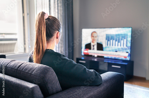 Tv news. Woman watching television broadcast in home living room. Reporter, anchor and studio host in screen with newscast headlines. Person sitting on couch. Politics channel on election morning.