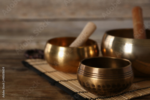 Golden singing bowls and mallets on wooden table, space for text