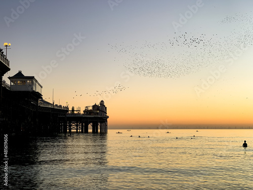 Beautiful sunset in Brighton. Starling murmuration at golden hour in English seaside. Beautiful sunset and birds flying above pier. Brighton Palace pier