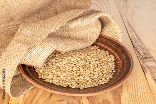 Dry organic green lentils with clay dish and burlap sack on wooden table.