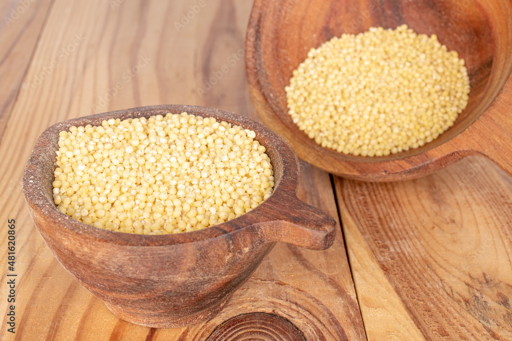 Dry organic millet in two wooden cups on a wooden table.