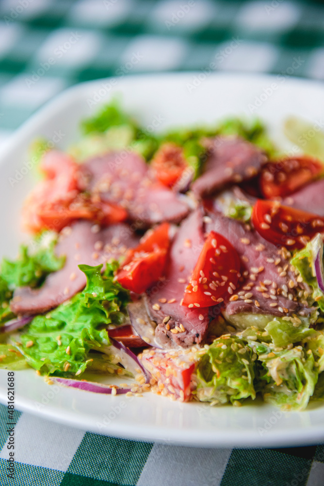 Healthy green salad with meat, tomato and lettuce served in a square white plate over green plaid tablecloth Healthy green salad with meat, tomato and lettuce served in a square white plate over green plaid tablecloth