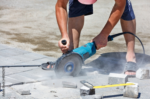 A worker on the street cuts paving slabs with a grinder with a diamond blade to make a sidewalk.