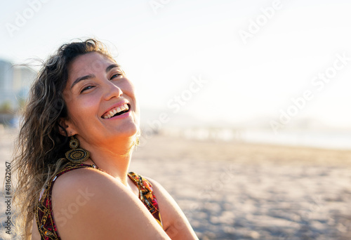 young latin woman sitting on the the beach smiling happy portrait