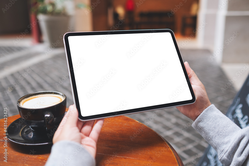 Mockup image of a woman holding digital tablet with blank white desktop screen with coffee cups on the table Mockup image of a woman holding digital tablet with blank white desktop screen with coffee cups on the table