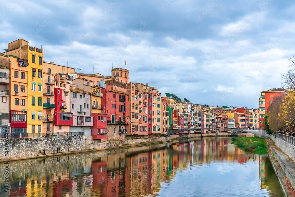 Landscape of Girona with Gomez or Princess Bridge over the river Onyar, Spain. Town panorama with bright multi-colored old houses and their reflections in the water stream