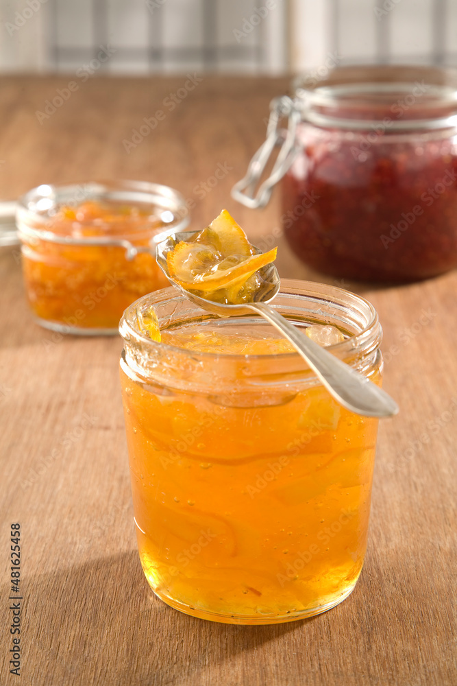 A spoon of marmelade on top of a jam jar, with strawberry and other jams in the background. A spoon of marmelade on top of a jam jar, with strawberry and other jams in the background.