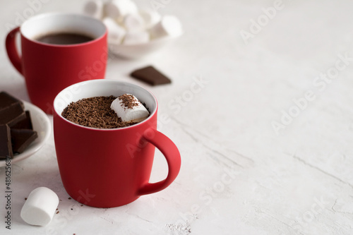 Homemade hot chocolate with marshmallows in a red cup on a light concrete background. Copy space.