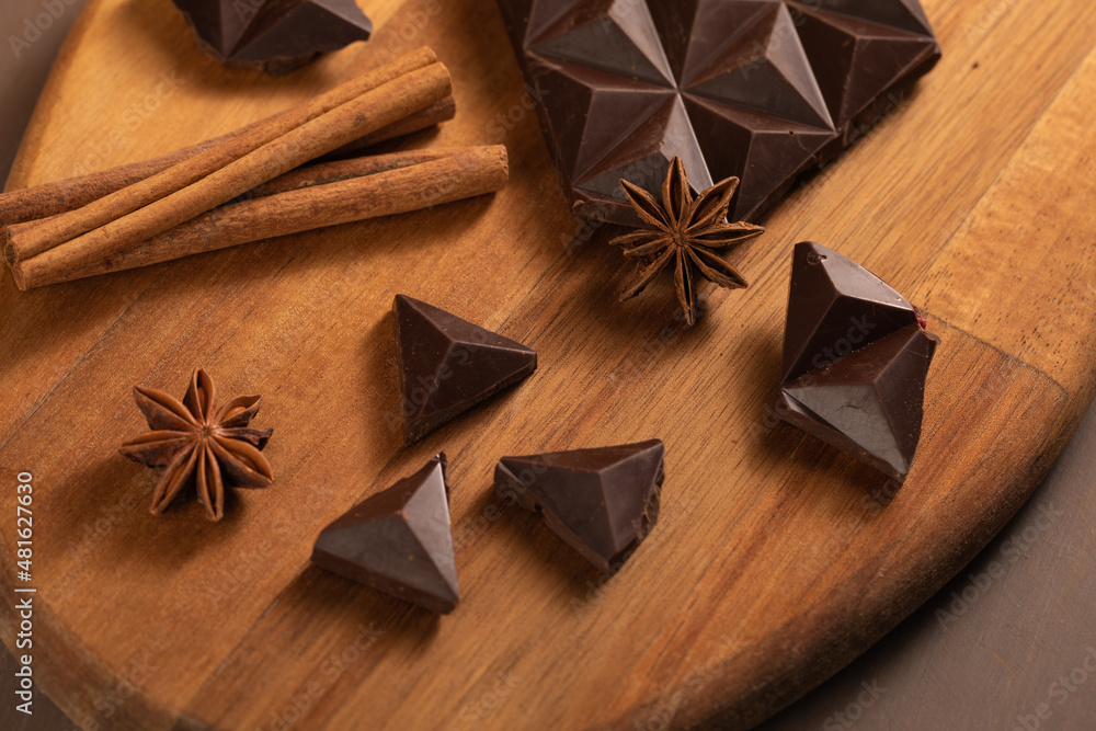 Dark bitter chocolate is broken into pieces. Decorated with cinnamon sticks. Brown background. Flatlay Dark bitter chocolate is broken into pieces. Decorated with cinnamon sticks. Brown background. Flatlay