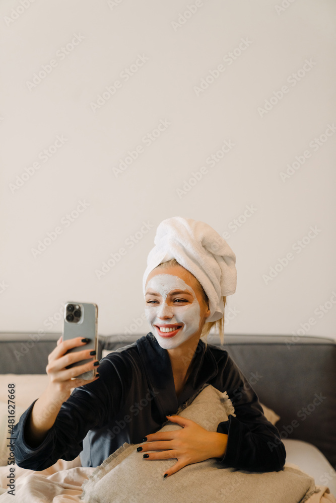 Young woman with face mask using mobile phone while sitting in bed Young woman with face mask using mobile phone while sitting in bed
