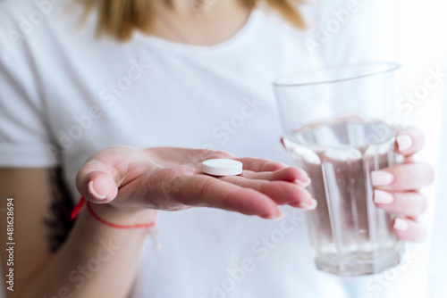 A young woman holds a glass of water and a pill for pain in the head or abdomen