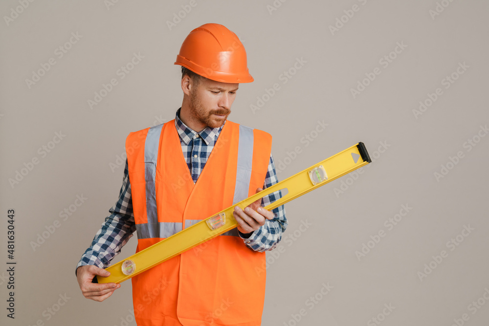 White man worker wearing helmet and vest posing with spirit level tool White man worker wearing helmet and vest posing with spirit level tool