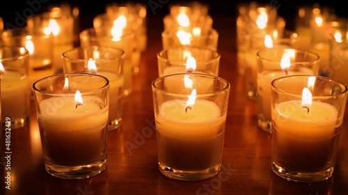 Camera moves past rows of glowing candles in a church or temple. photo