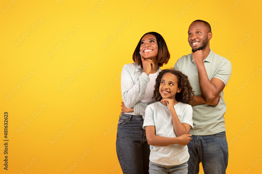 Special offer. Young black family of three looking aside at free space and holding hands on chin, yellow background Special offer. Young black family of three looking aside at free space and holding hands on chin, yellow background
