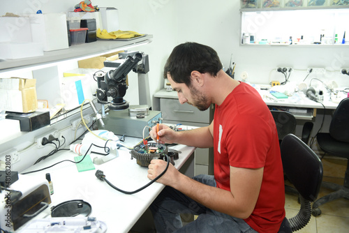 a young man in the workshop repairs an electrical appliance at his desk sitting in an armchair