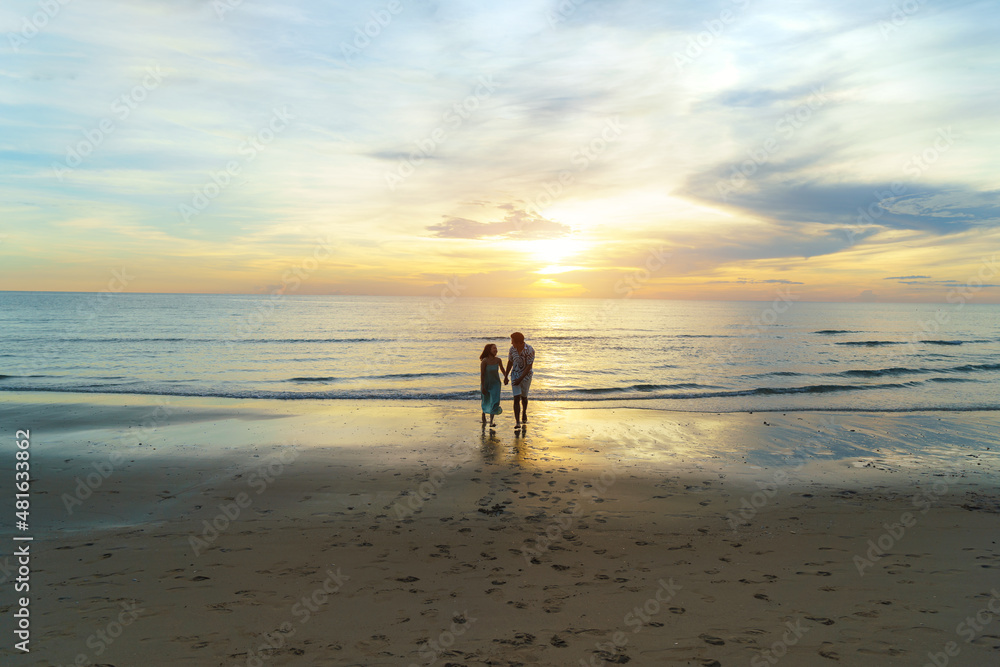 Naklejka premium Asian woman traveler holding man's hand and looking beautiful sunset on the beach, Couple on vacation in summer and freedom concept