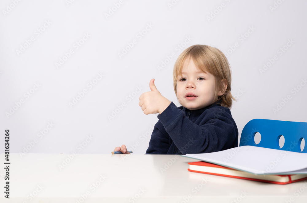 Little boy sitting at the table showing thumb up isolated over white background. Little boy sitting at the table showing thumb up isolated over white background.