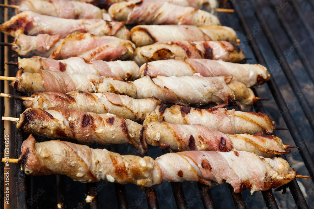 Meat wrapped in bacon on wooden skewers is grilled.