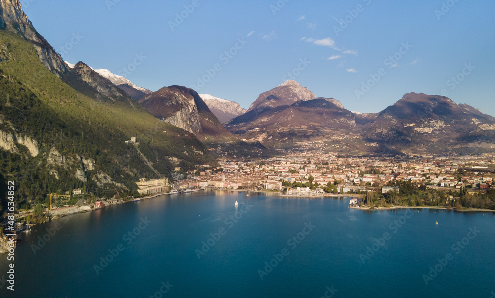 A strip of wooded and rocky mountains with a city near the shore of the lake against the blue sky