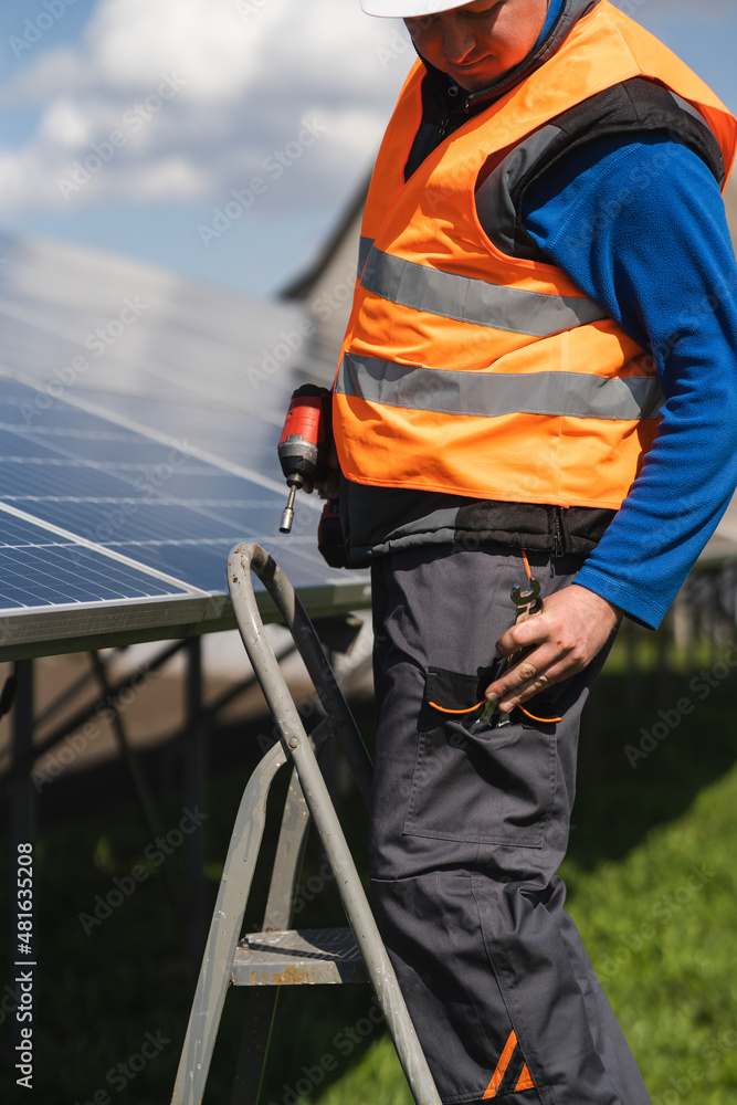 Male engineer who installs and maintains solar panels stands on a stepladder and takes out a wrench from his pocket