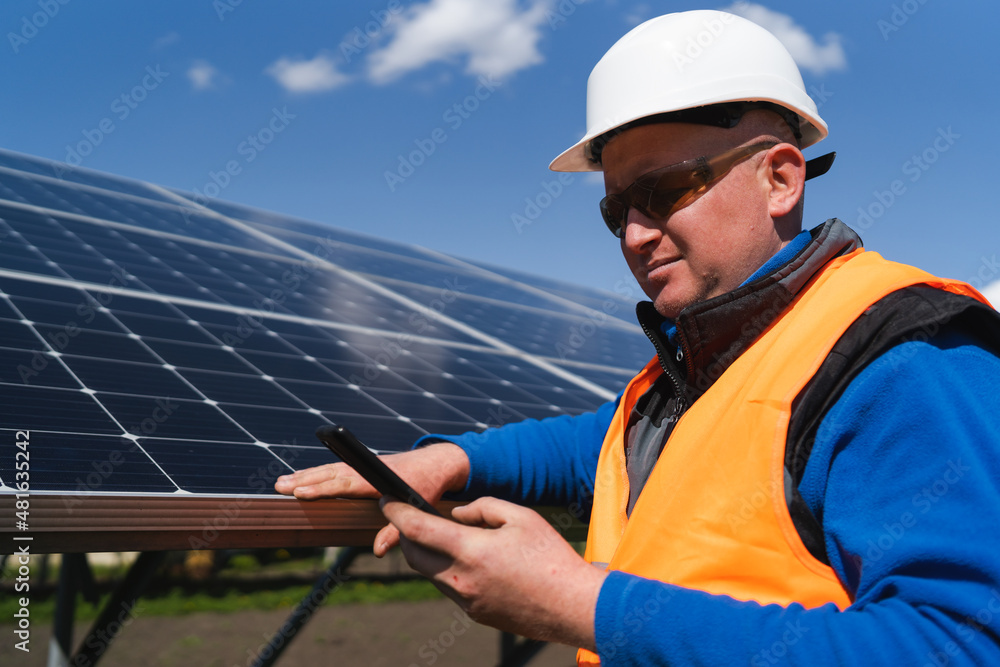 Man in hard hat using smartphone on the background of solar panels Man in hard hat using smartphone on the background of solar panels