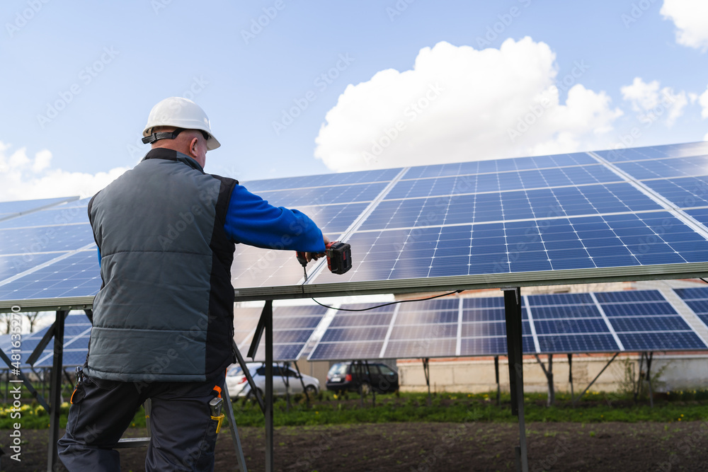 Back view of a man works with a drill screwdriver on solar panels Back view of a man works with a drill screwdriver on solar panels