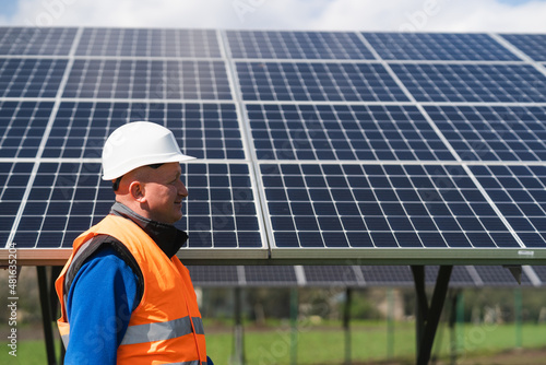 Engineer in work clothes and helmet walks through a solar power plant against the backdrop of panels