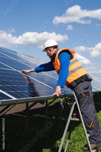 Solar power plant worker on stepladder makes a visual inspection of solar panels