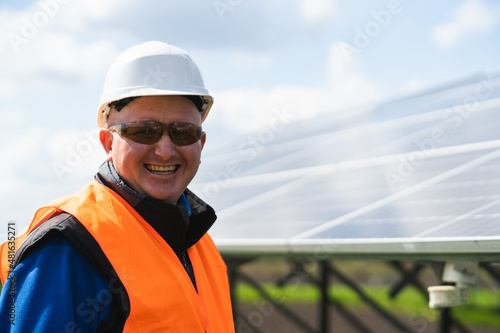 Close up portrait of engineer in a hard hat and protective glasses on a farm with solar panels © Andrii 