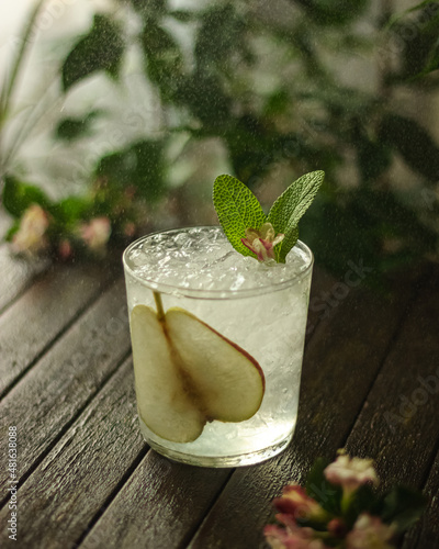 summer cocktail decorated with mint, lemon and slices pears on a wooden table on a floral background