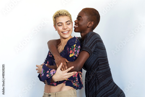 Photo of joyful ladies kissing and embracing togetherness, being of different of races, dressed in casual clothes.