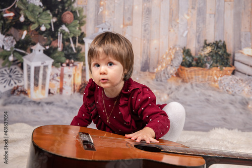 Kleinkind sitzt vorgebeugt bei Gitarre, neugierig blickend photo