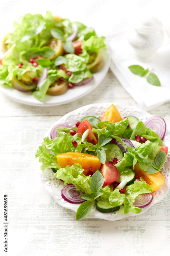 Salad with red and yellow Tomatoes and Pomegranate Seeds on bright wooden Background. Close up. Salad with red and yellow Tomatoes and Pomegranate Seeds on bright wooden Background. Close up.
