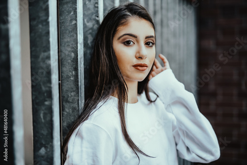 worried teenager girl with hand at head look at camera think about being a bullied victim and stand confident in front of fence