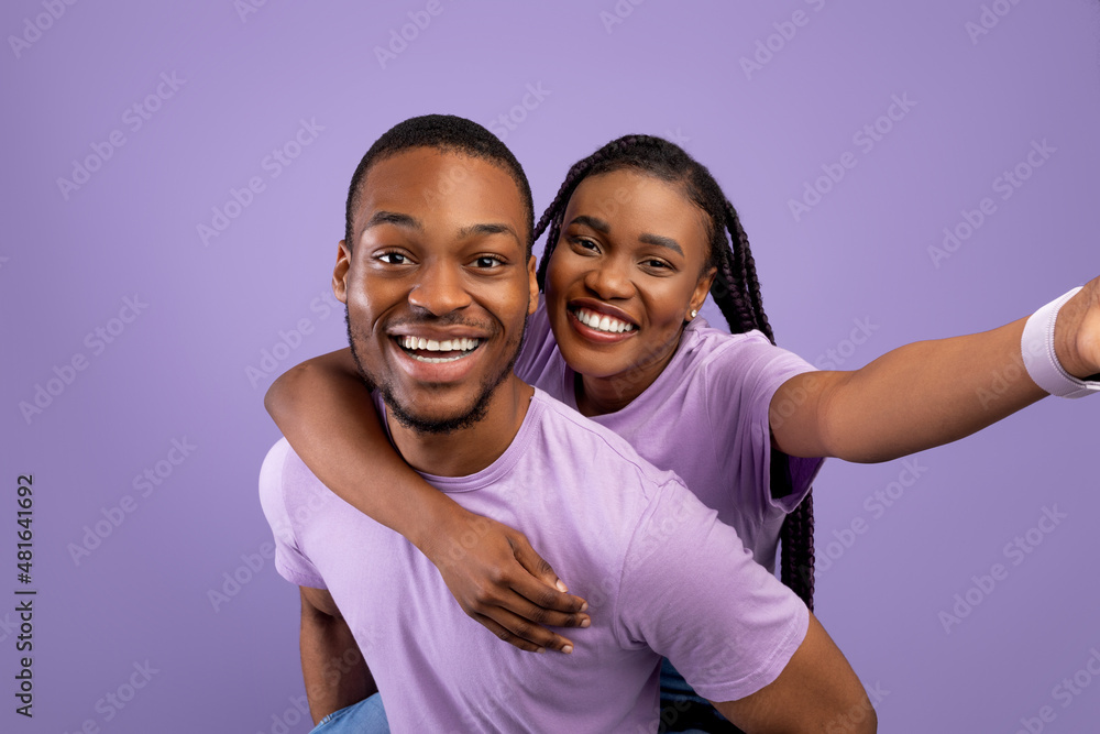Obraz premium Black couple taking selfie, woman riding on guy's back